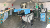 Das Bild zeigt einen mobilen medizinischen Einsatzbereich mit medizinischem Equipment und einer Medi-Help OP-Liege in einem Zeltraum.