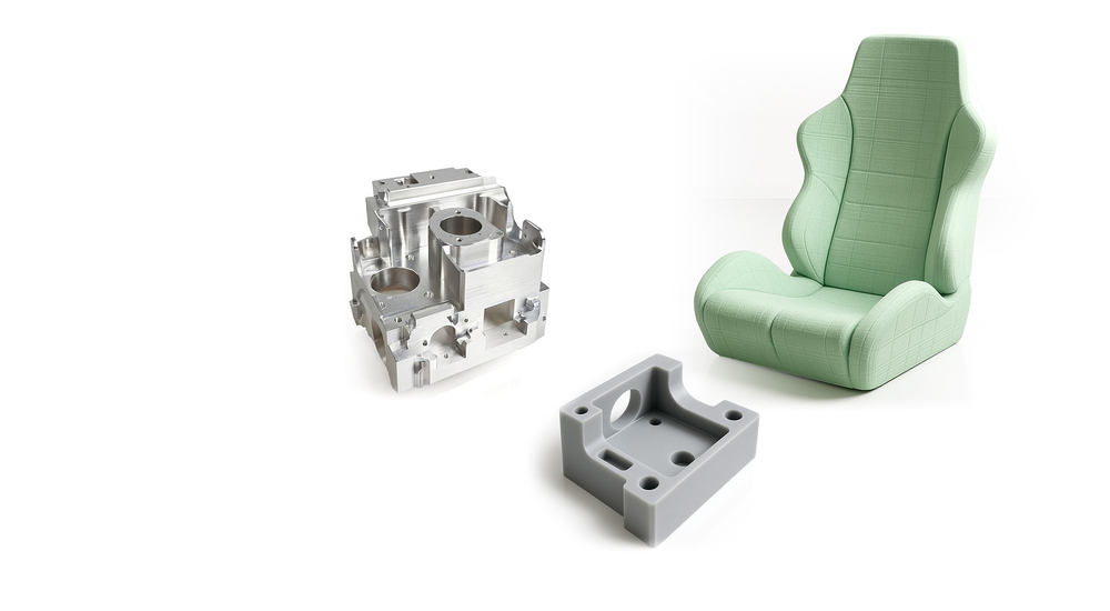 Auf dem Bild sind verschiedene Teile zu sehen: ein bearbeitetes Metallteil, eine graue Kunststoffform und ein gepolsterter Sitz.