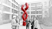 Auf dem Bild ist eine Gruppe von fünf Personen in einem Innenhof zu sehen, die vor einer großen roten Skulptur stehen und miteinander sprechen.