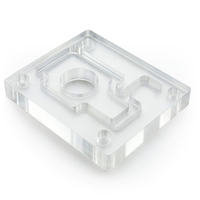 Auf dem Bild ist ein transparenter, klarer Kunststoffblock mit einer bearbeiteten Form und mehreren Gewindebohrungen zu sehen.